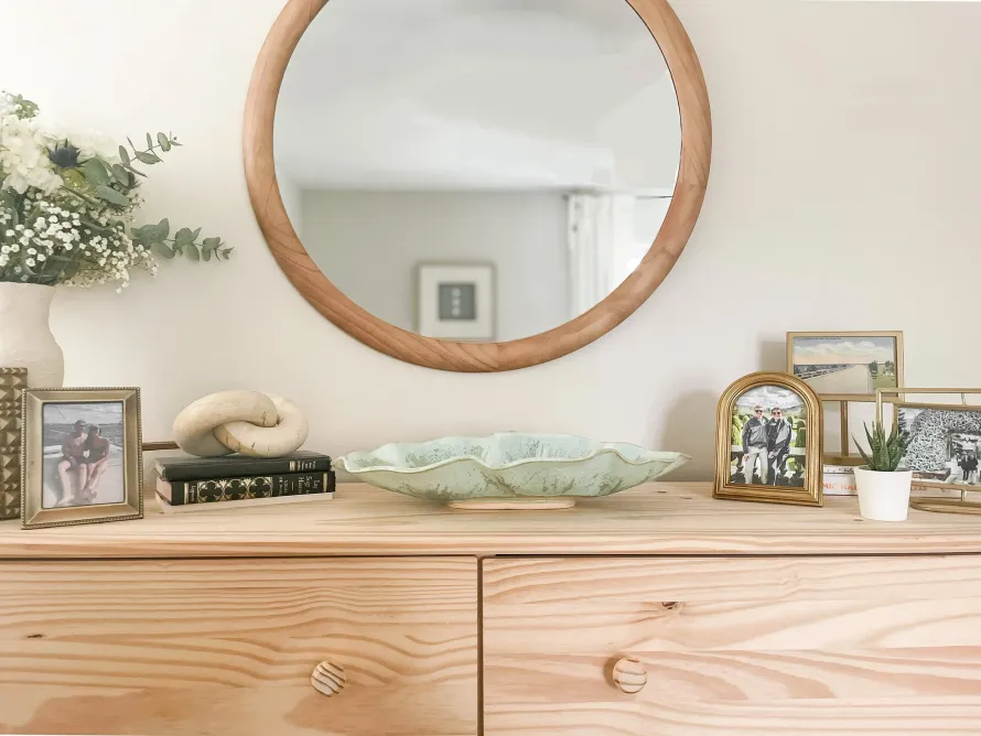 A bedroom dresser styled with a mirror above it, layered with a small framed artwork and a ceramic vase, creating a collected and personal look