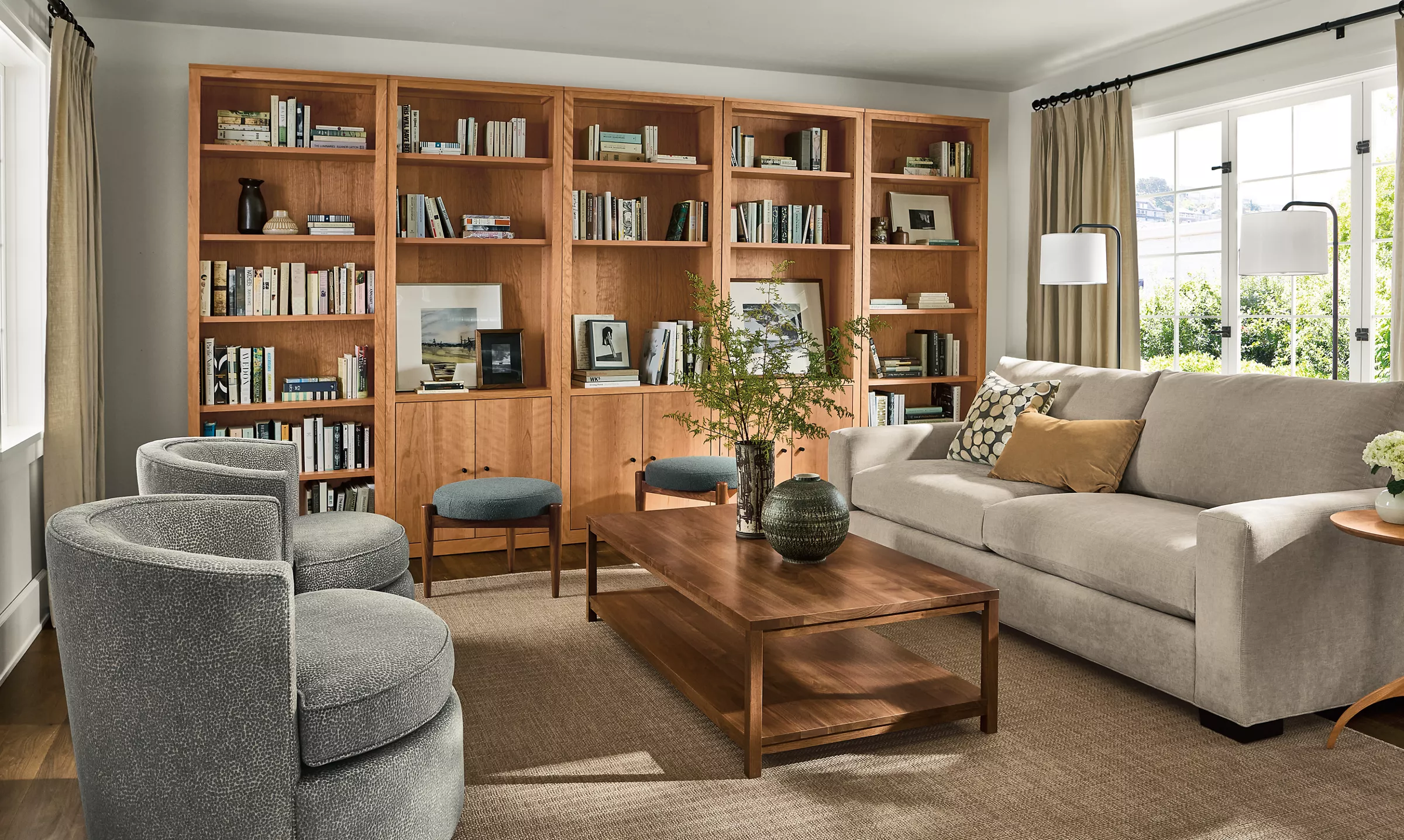 A bright living room with a light oak coffee table, a medium walnut sideboard, and dark stained picture frames, styled with a neutral rug and warm textiles