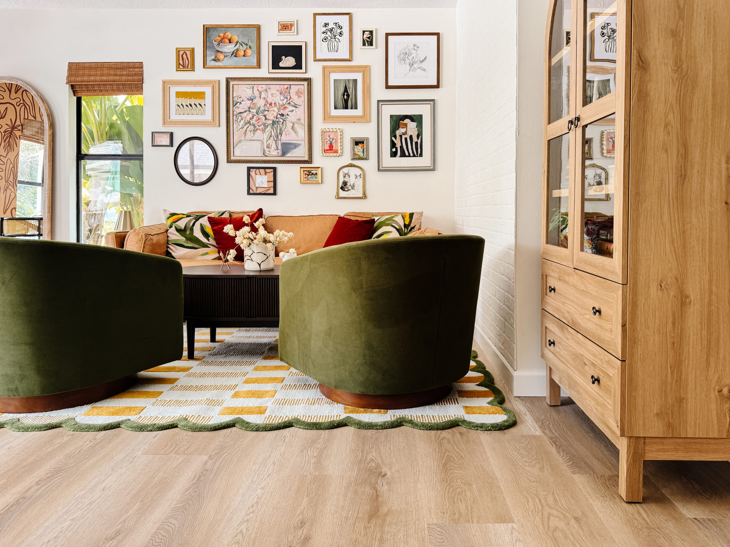 A colorful eclectic gallery wall with mixed frame finishes and bold art prints above a neutral sofa in a bright apartment