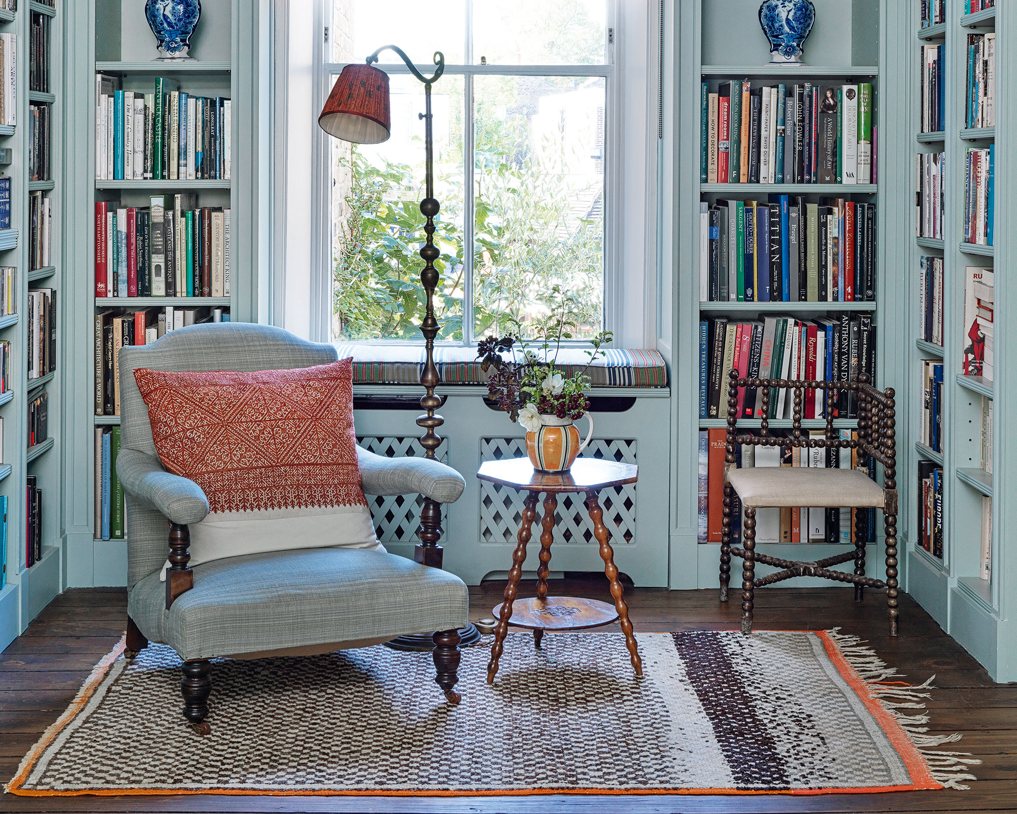 A cozy reading corner with a woven basket holding blankets and books next to an armchair, with a small side table and warm lamp light