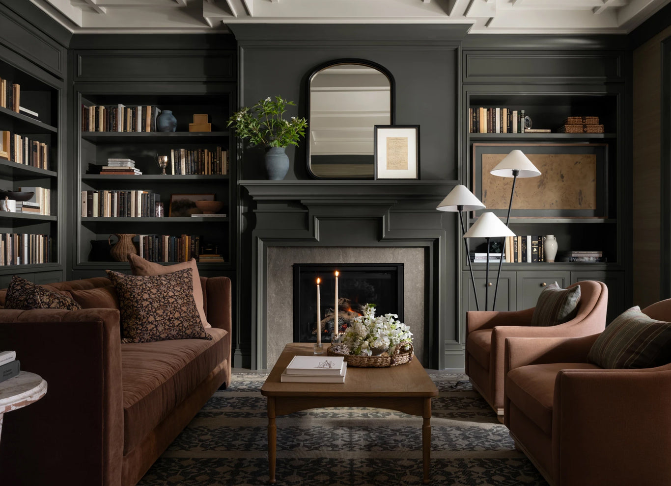 A moody living room with deep-colored walls, a glowing table lamp on a sideboard, and a floor lamp brightening the seating area