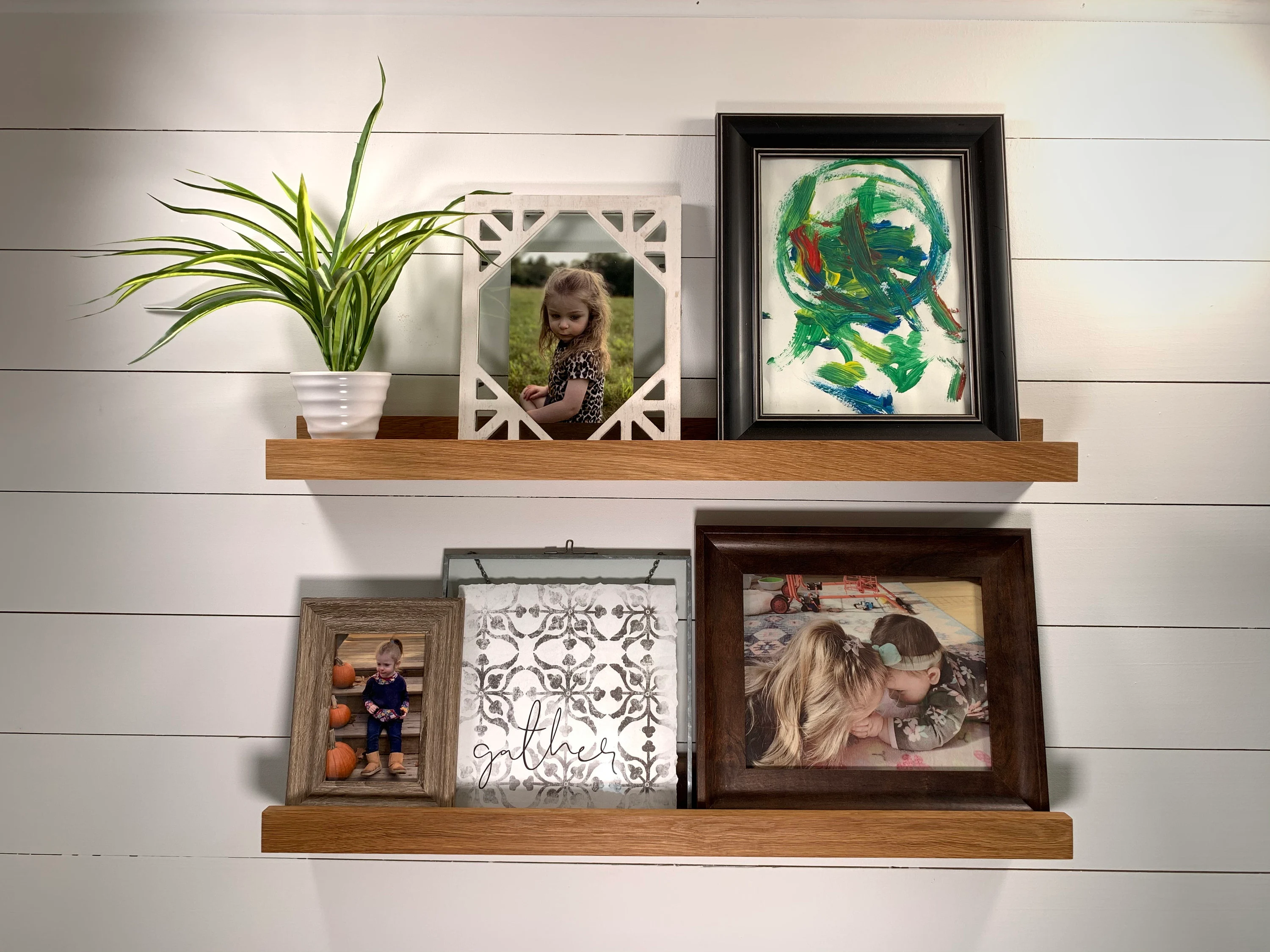 A narrow display ledge mounted on a wall holding layered frames and a small vase, styled in a calm neutral palette
