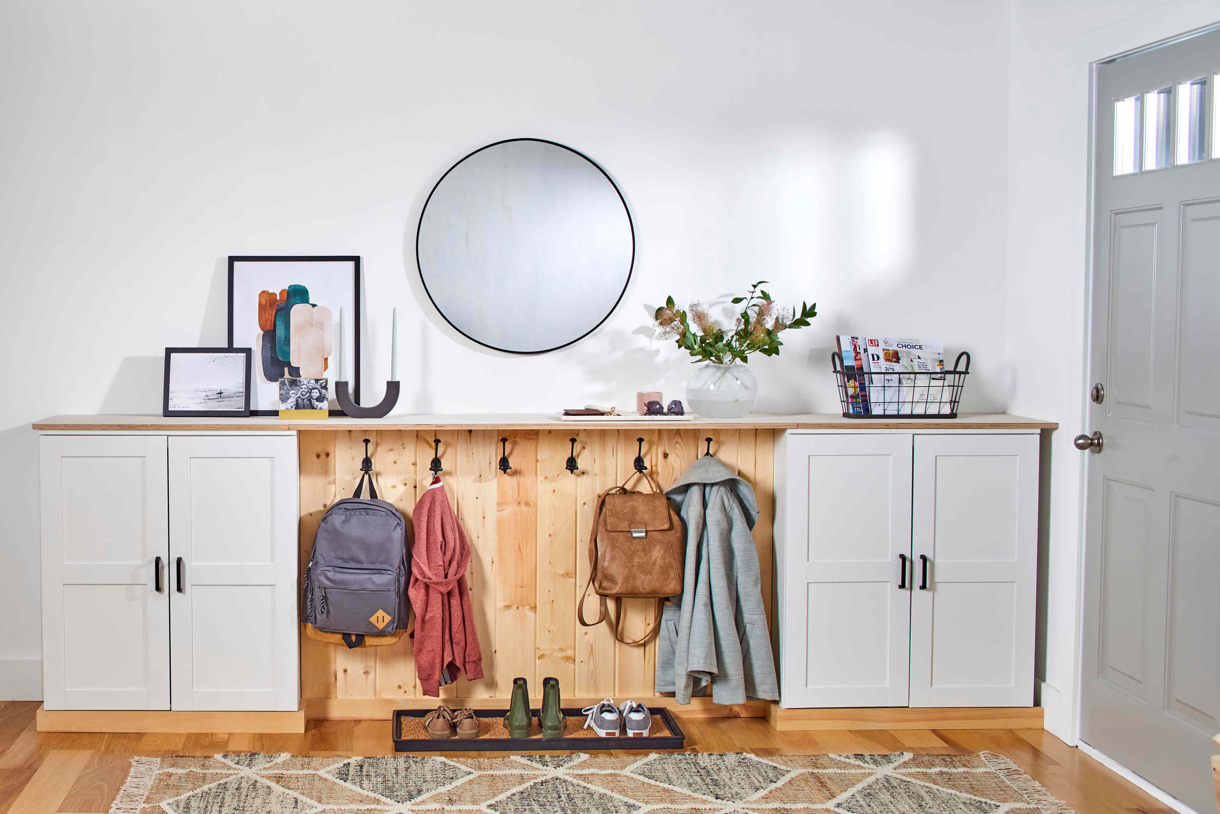 A narrow hallway entry with three matte black wall hooks above a slim floating shelf holding a small tray for keys, with a light neutral wall and a simple runner rug