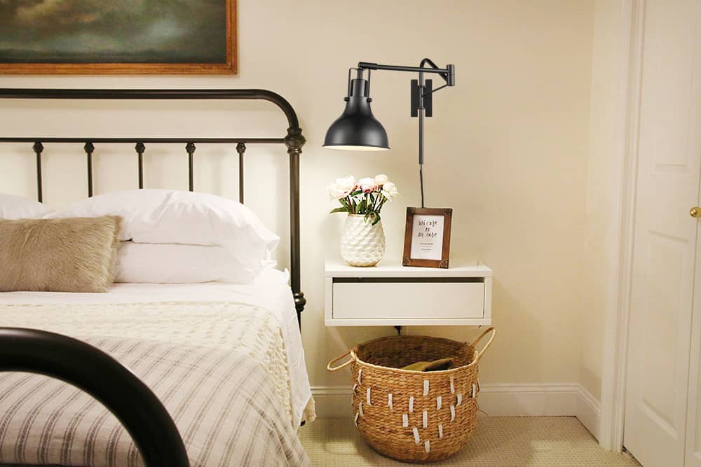 A reading corner with a plug-in wall sconce mounted above a chair, casting warm light over an open book on a small side table