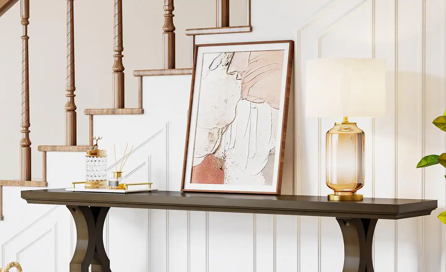 A set of framed artworks leaning against a wall on a narrow console table, layered with a ceramic vase and a small stack of books