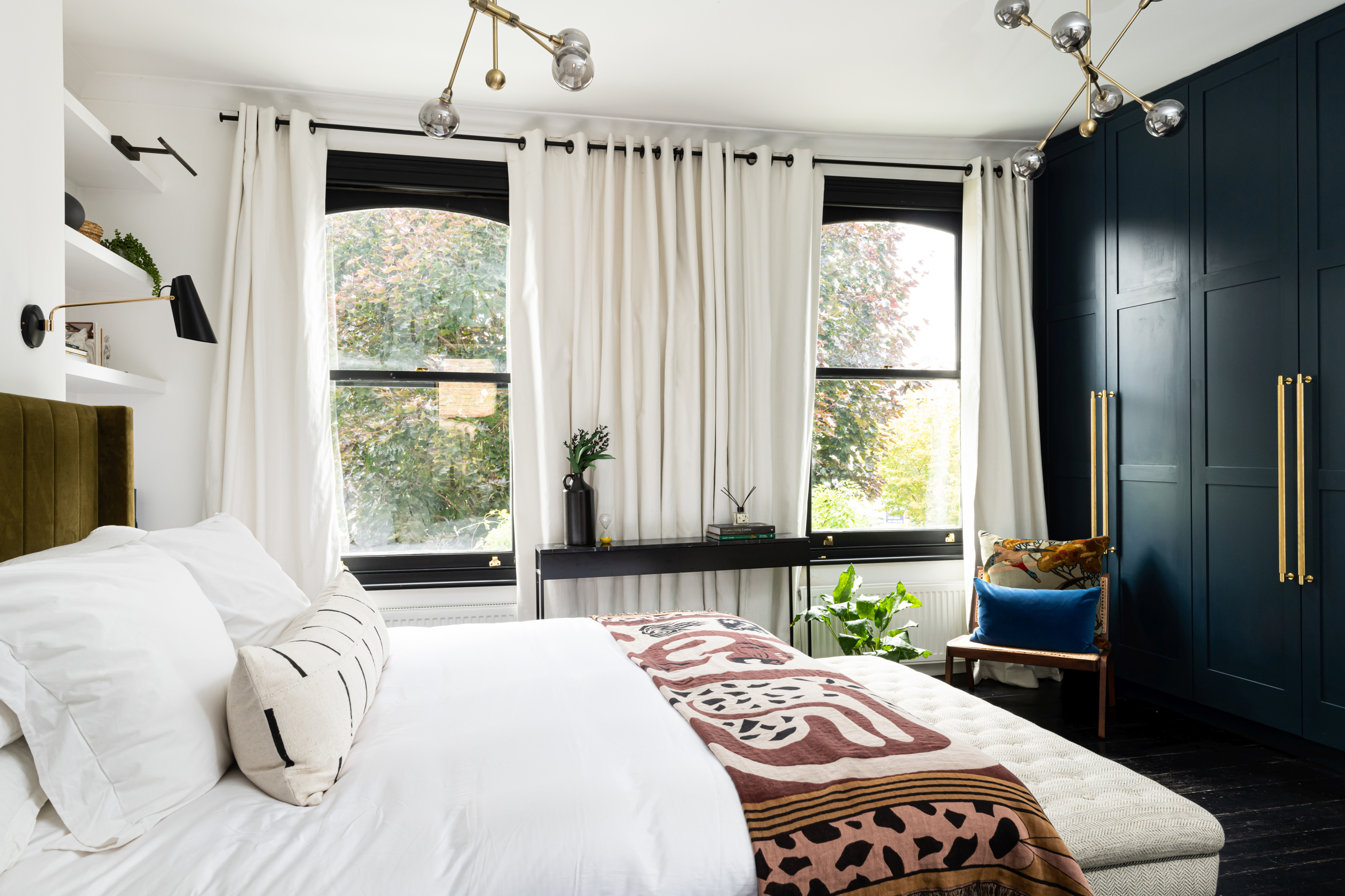 A small bedroom with curtain panels hung close to the ceiling and draping to the floor, making the window wall appear taller