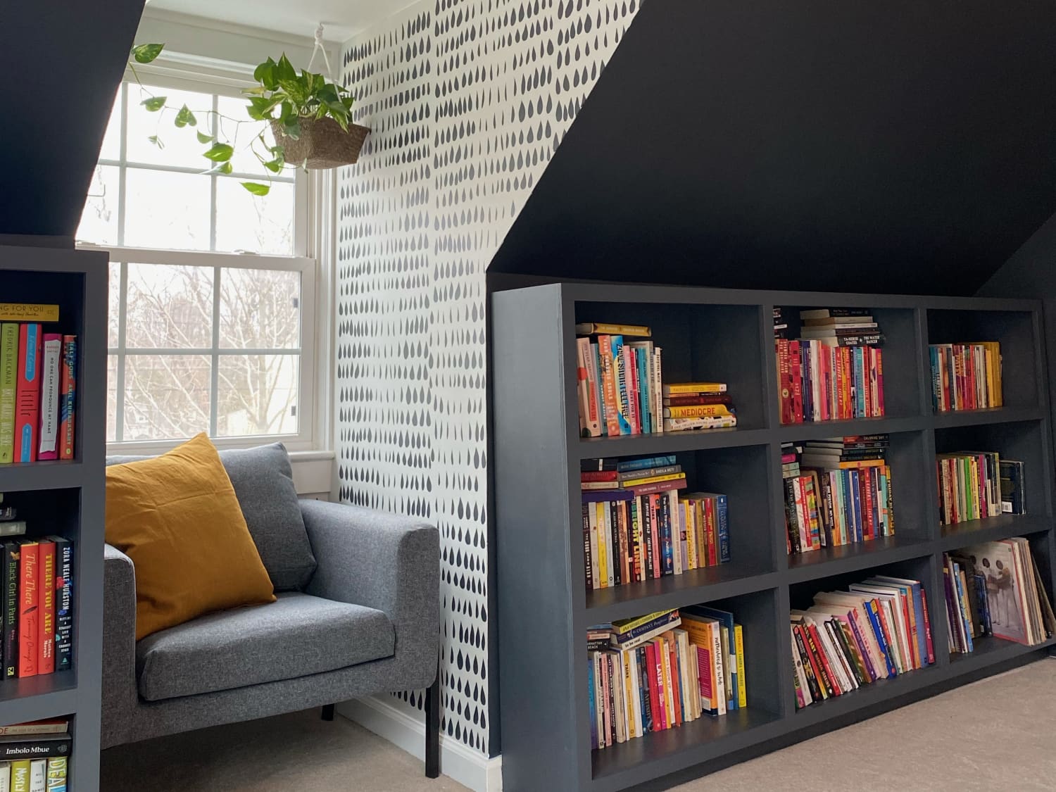A small studio apartment reading nook with a compact chair, a wall-mounted shelf holding a mug and books, and a plug-in sconce creating warm focused light