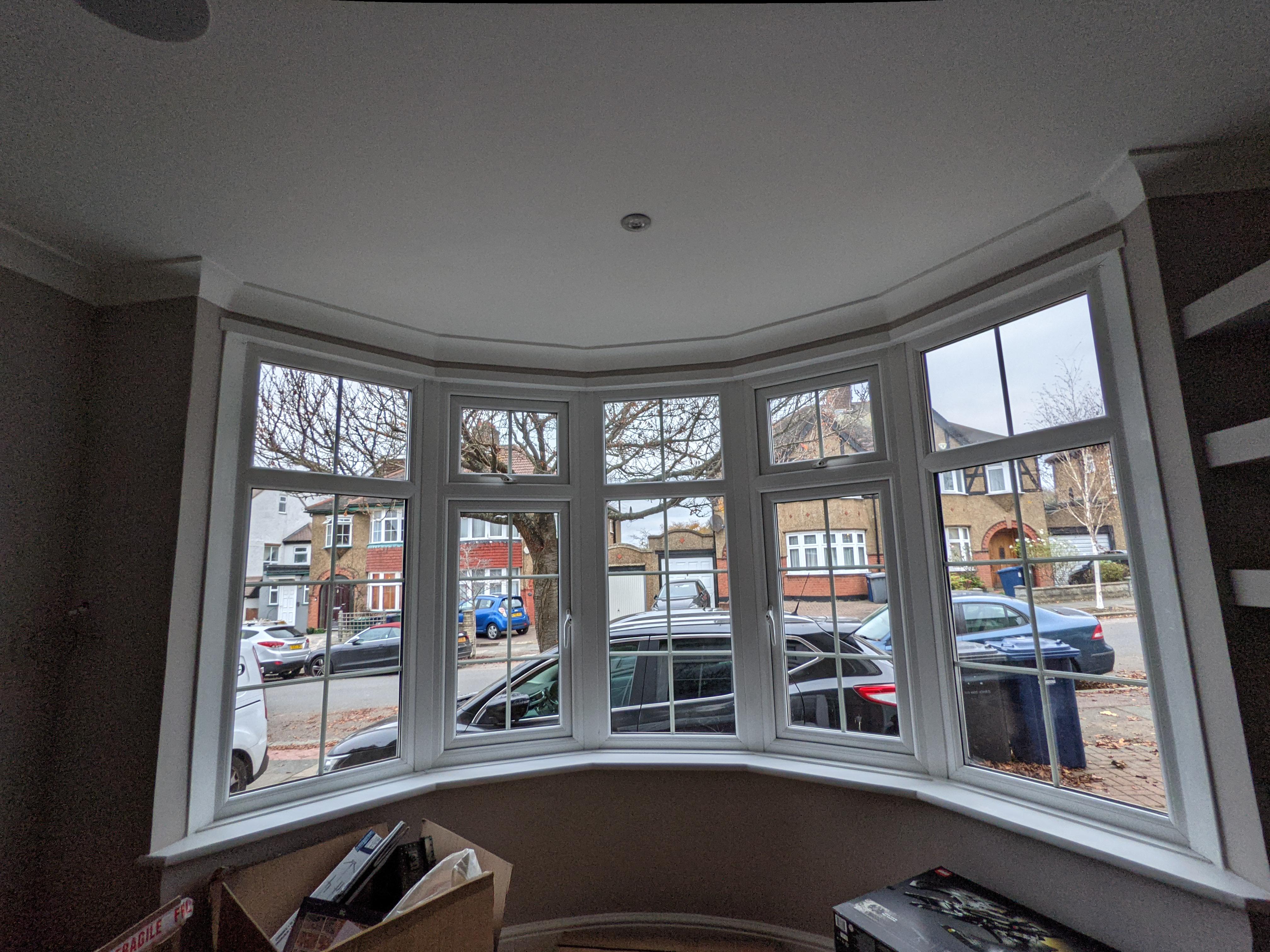 A sunlit bay window with a ceiling-mounted curtain track and long panels that frame the window and fall neatly to the floor