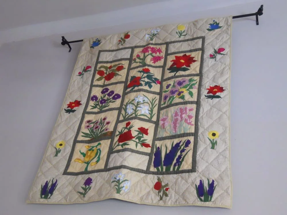 A vintage quilt hung flat on a living room wall above a simple bench, adding texture and warmth