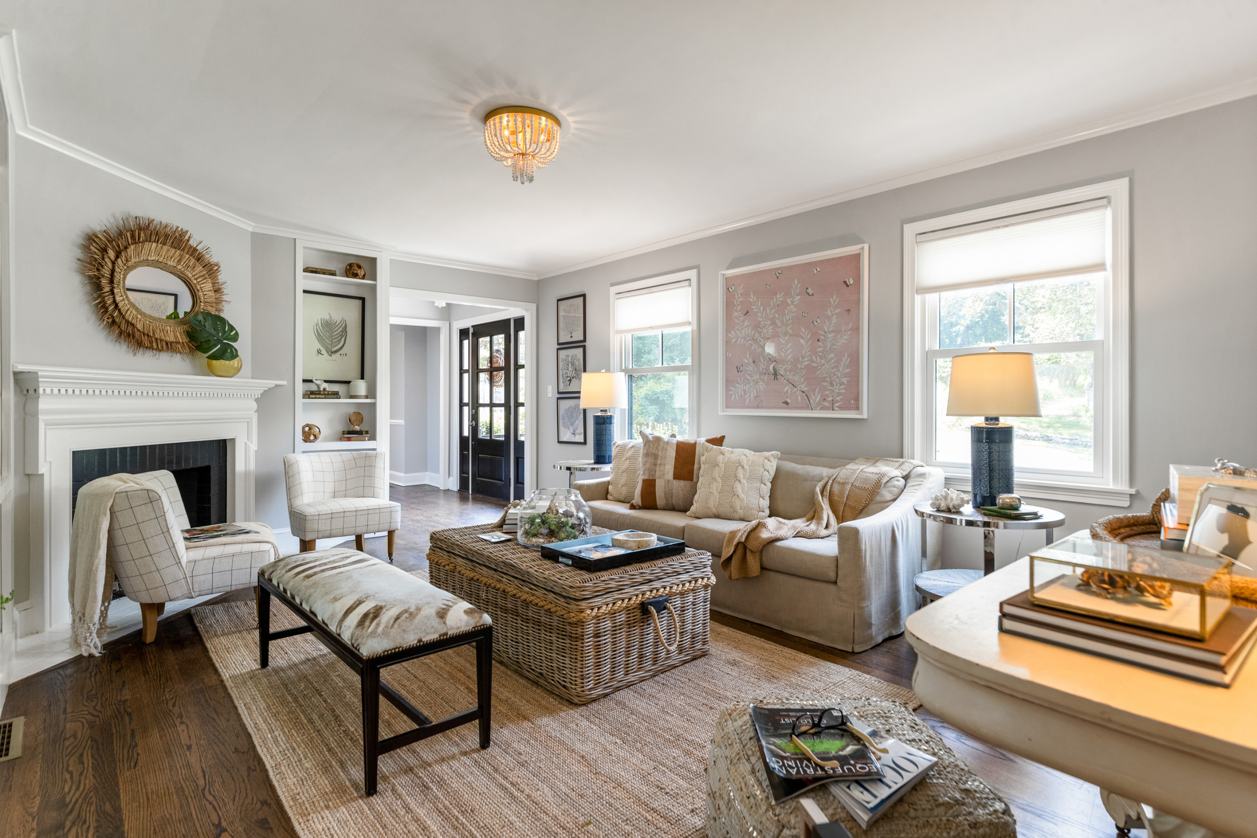 A warm, inviting living room at dusk with a ceiling light on low, a floor lamp beside the sofa, and a small table lamp glowing on a sideboard