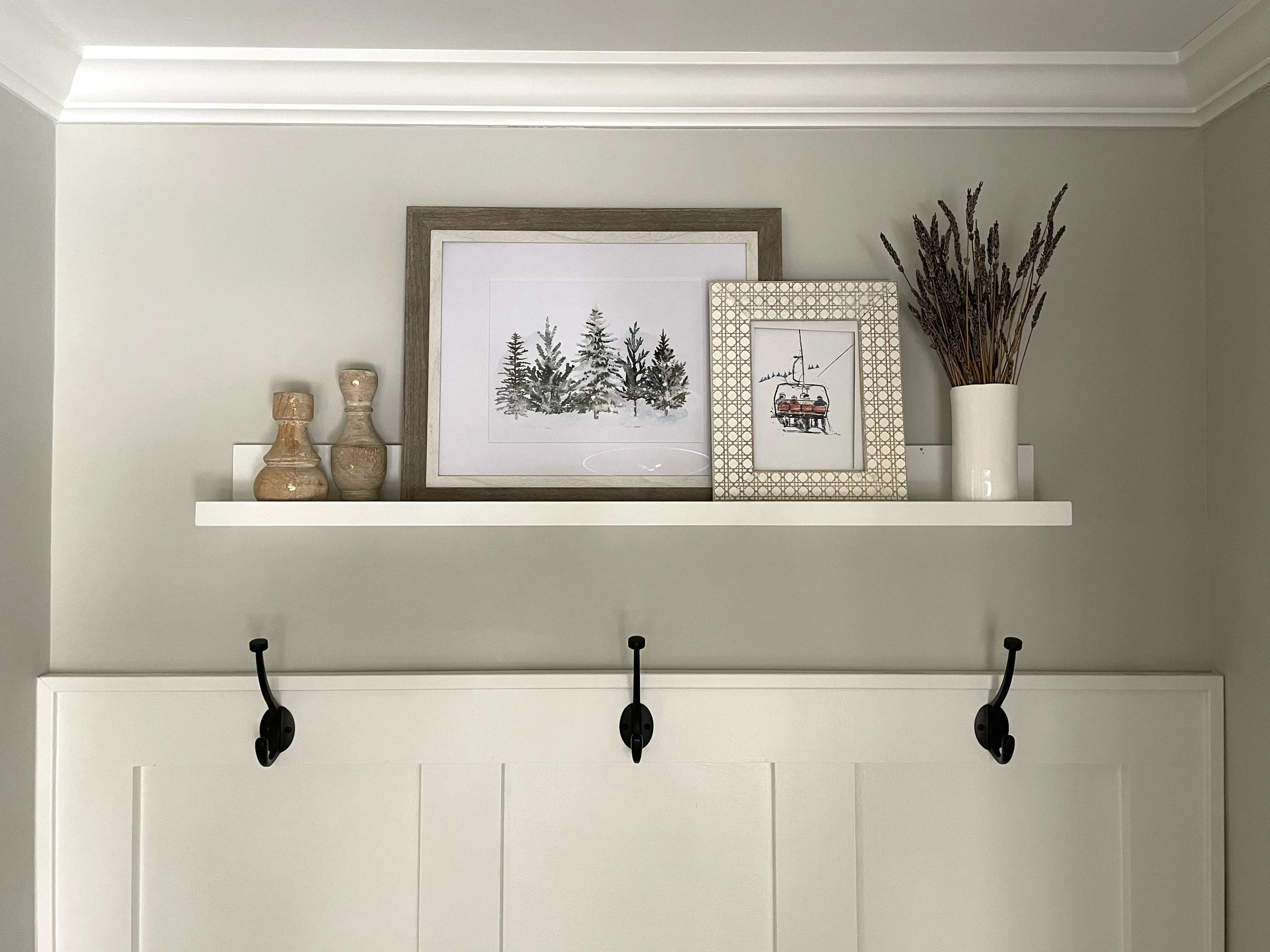 A white picture ledge shelf holding layered frames and a small ceramic sculpture against a warm neutral apartment wall